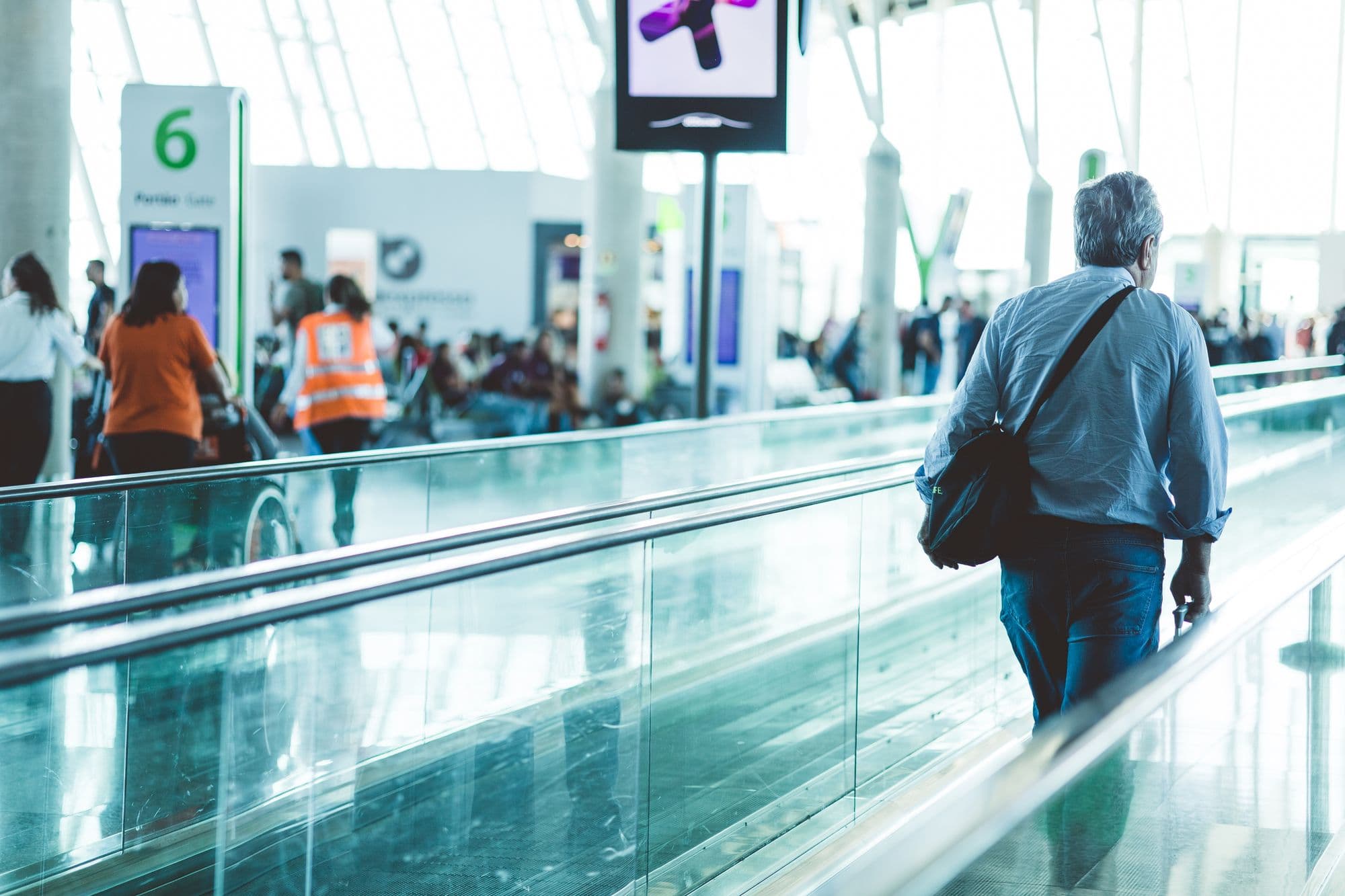 Travellers moving along a walkway in a bright, modern airport terminal
